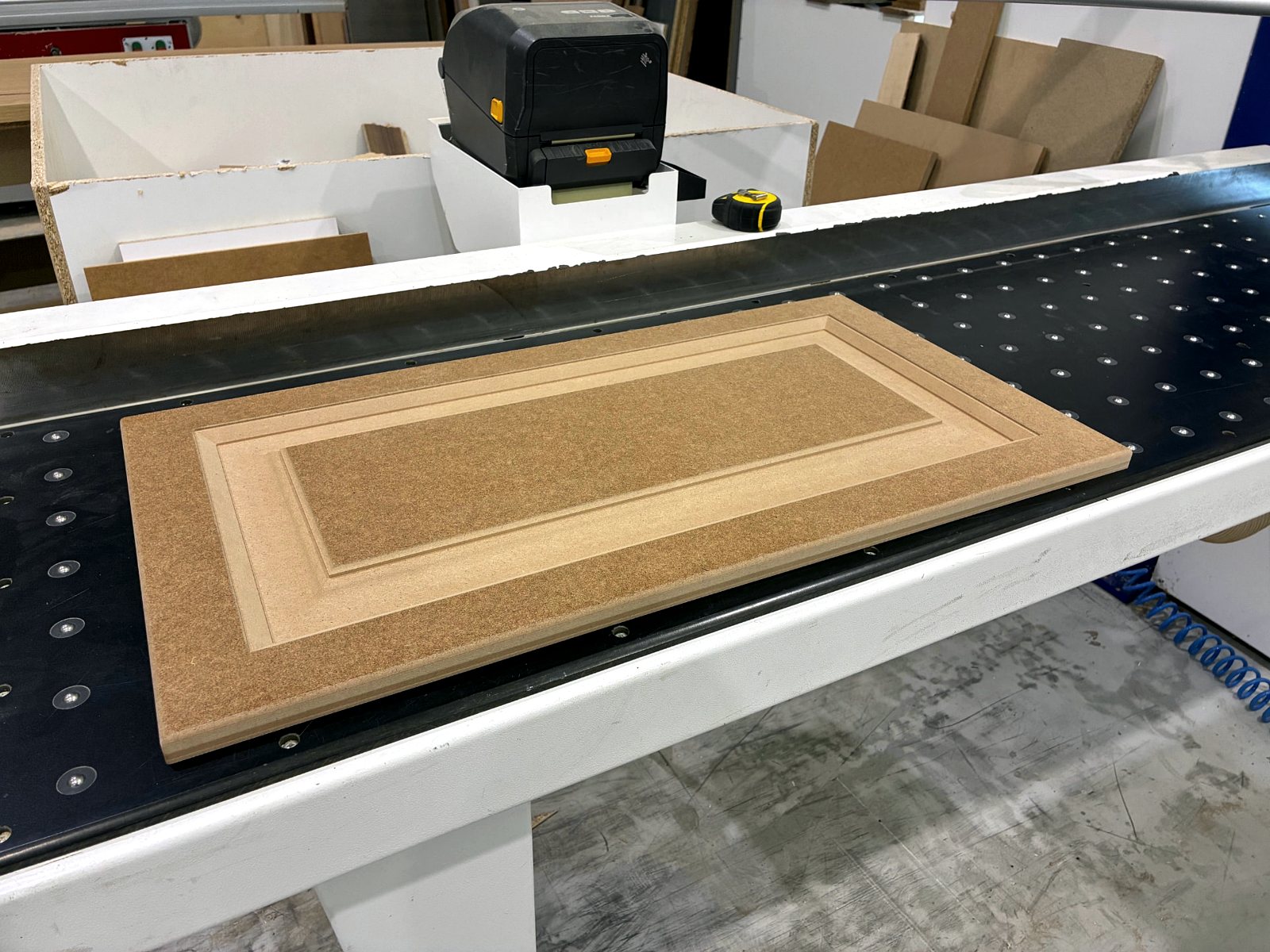CNC-vel mart fehér MDF konyhafrontok egymásra rakva a műhelyasztalon